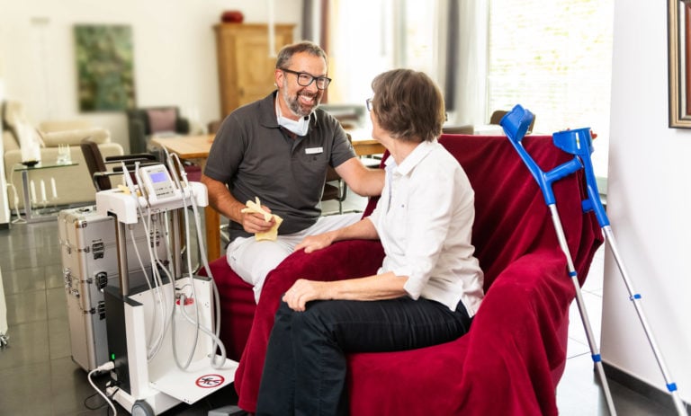 Zahnarzt spricht mit Patientin während Behandlung im Behandlungsraum, moderne Geräte sichtbar.